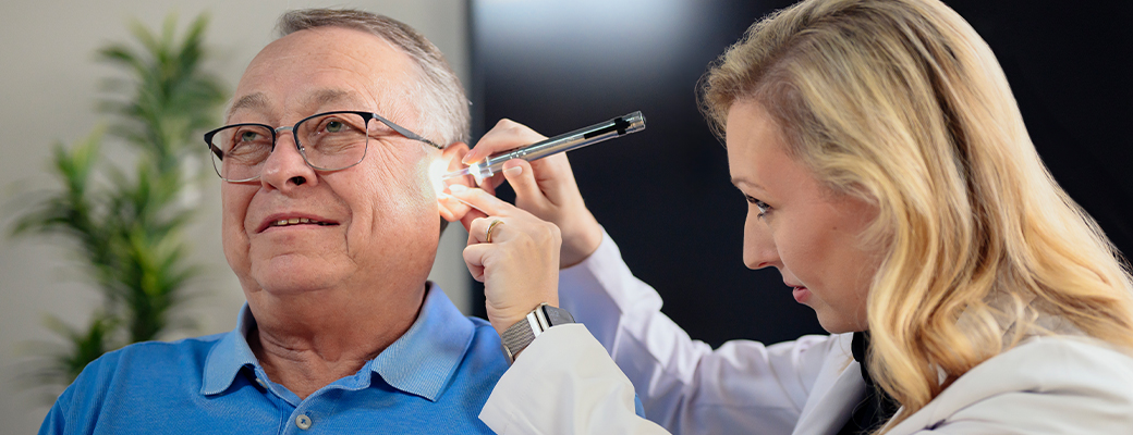 Image of female hearing care professional shining a light into ear of senior male patient